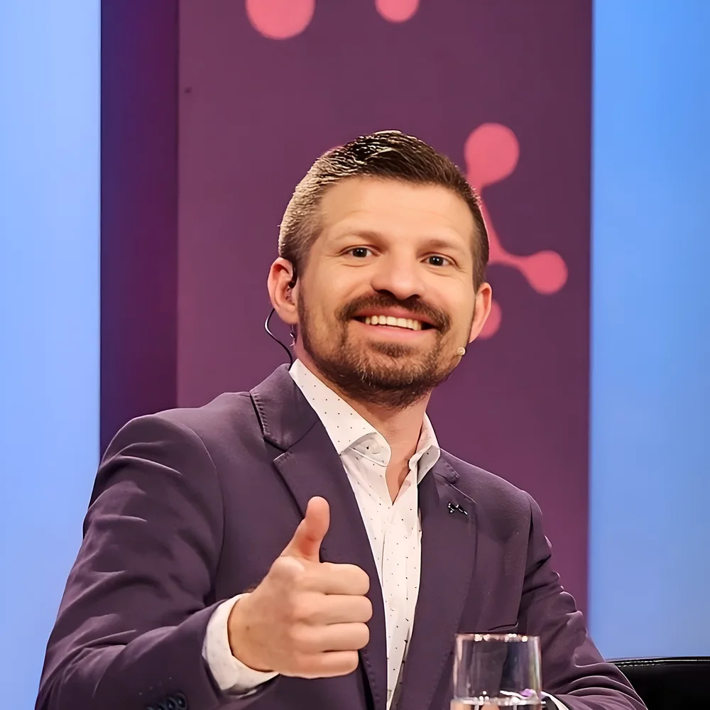 Konrad Peschka sonriendo en el set de televisión, haciendo un gesto de pulgar arriba